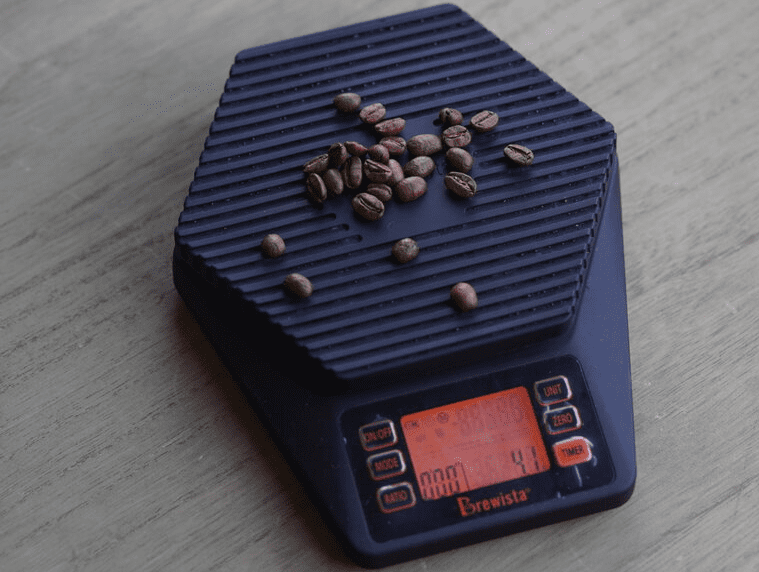 La mano de barista está poniendo granos de café en una báscula digital para  medir el peso tostado ligero